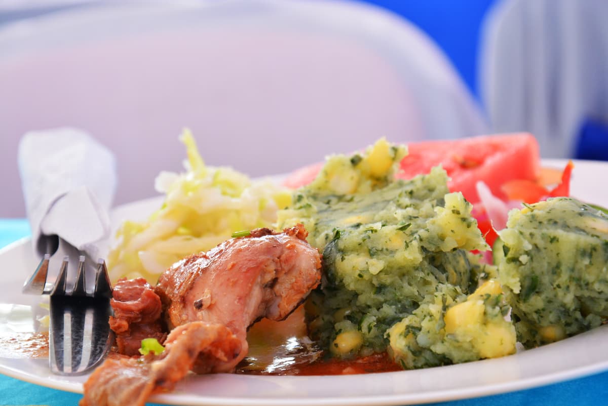 Green mashed potatoes with corn beside stewed meat, cabbage, and tomato on a white plate.