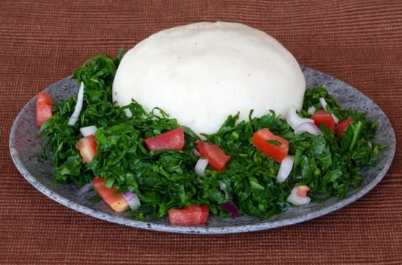White maize porridge served with sauteed leafy greens on a plate.
