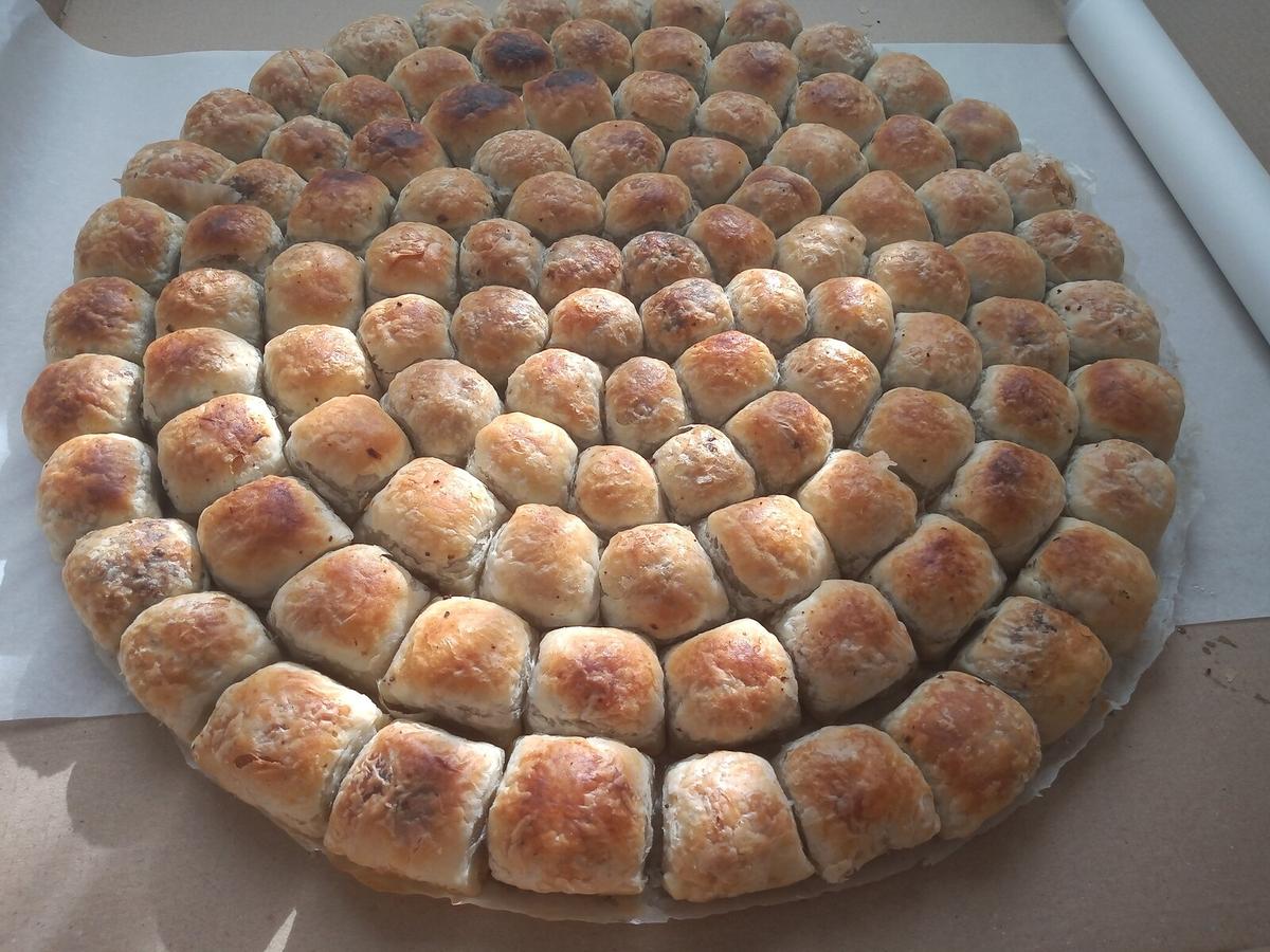 Rundes Blech mit kleinen braunen, mit Fleisch gefüllten Teigstücken.