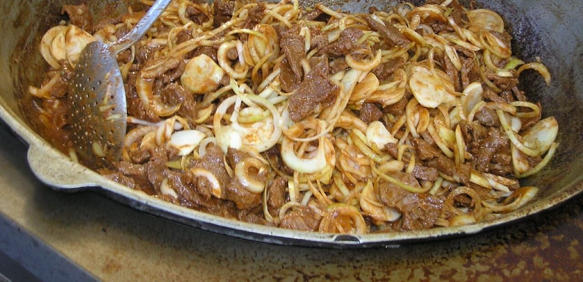 Gebräuntes Fleisch und Zwiebelscheiben garen in einem breiten Metalltopf.