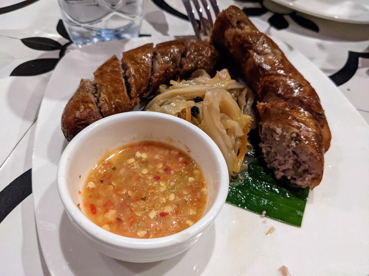 Gegrillte Kräuterwurst auf einem schlichten Teller mit einer kleinen Schale Dip.