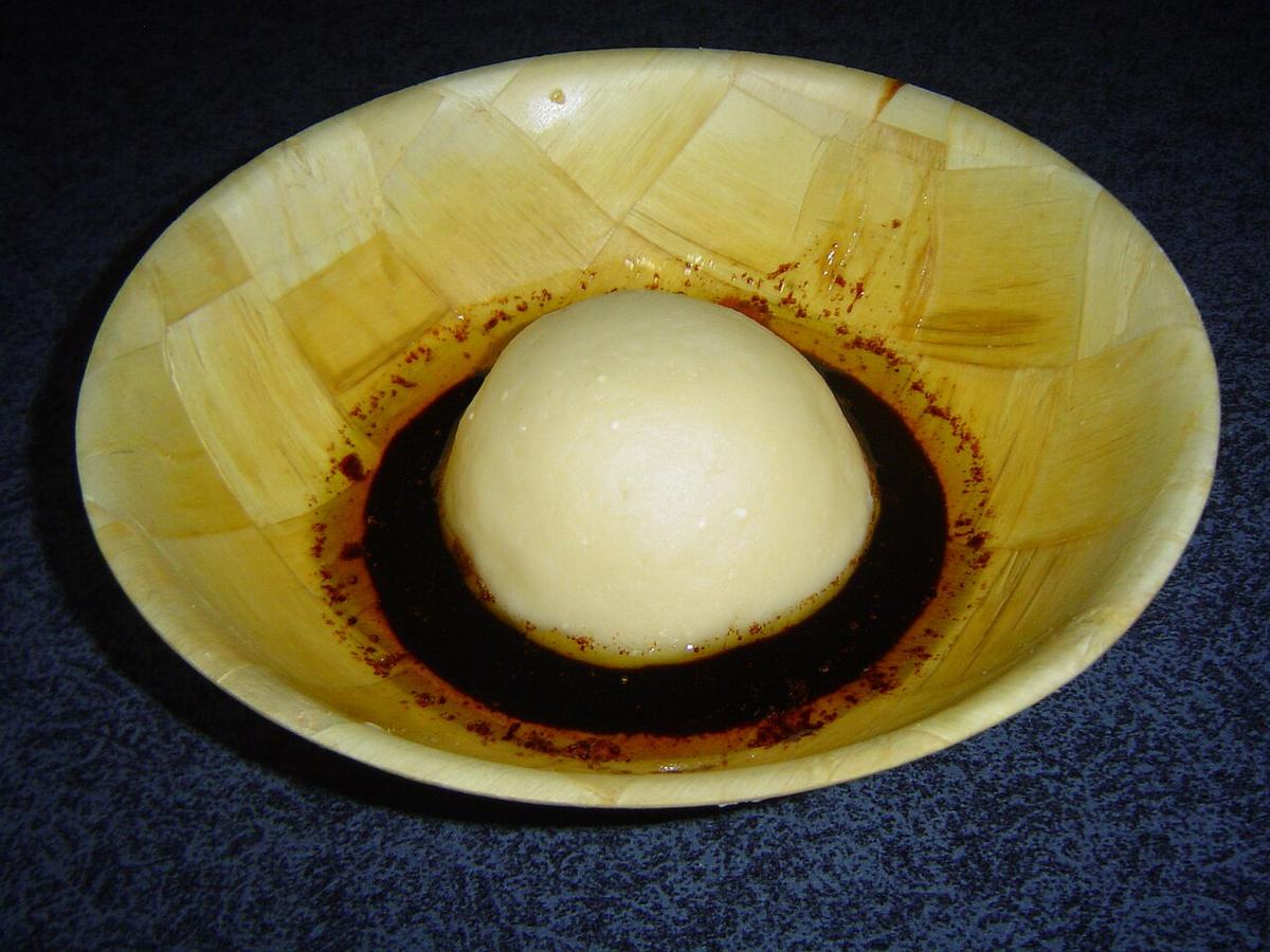 Glatte, helle Mehlkuppel in einer Schüssel mit dunklem Sirup darum.