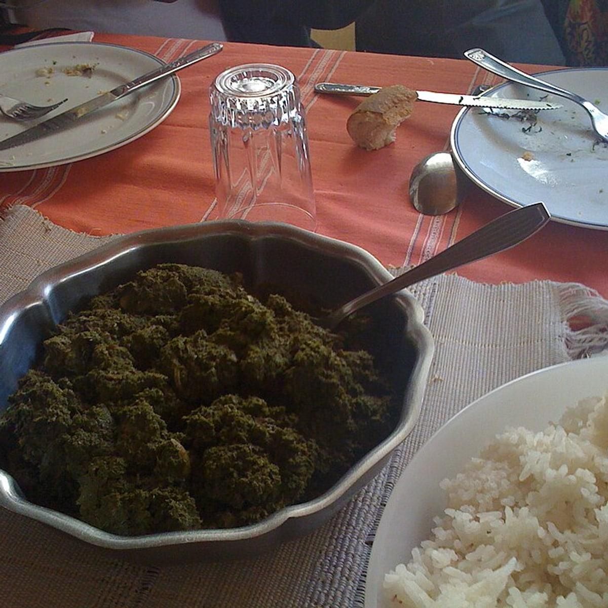 Dark cassava-leaf stew in a pot with rice on the side.