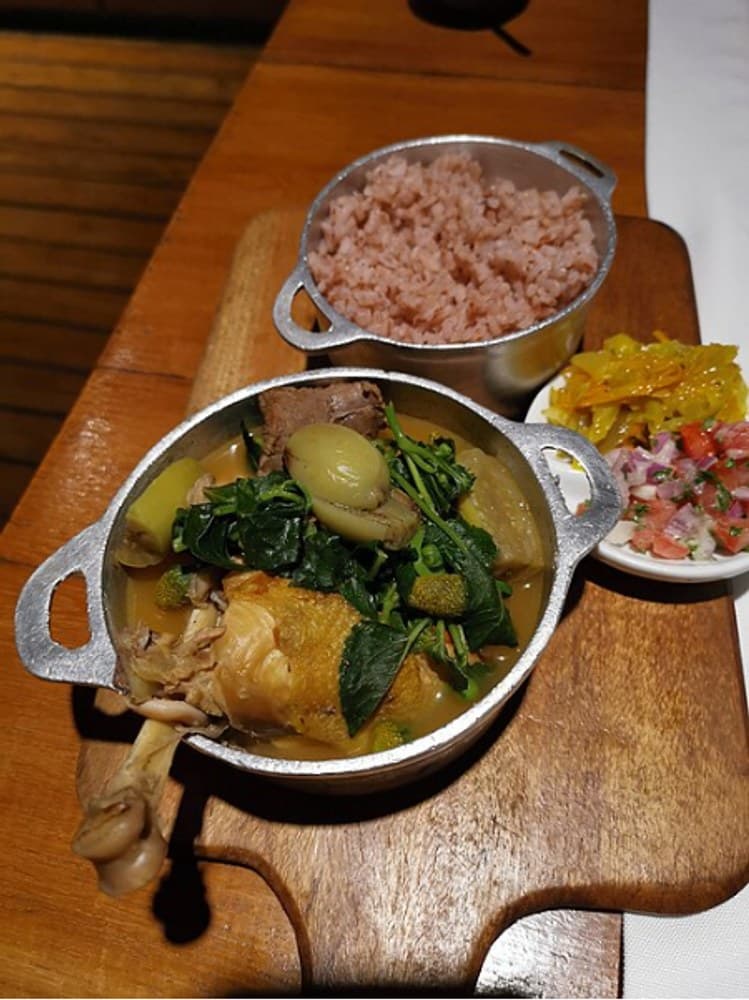 Small pot of meat and greens stew served beside a pot of rice.