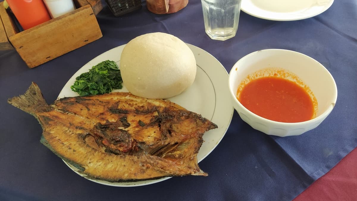 Gumpalan pati singkong bulat disajikan dengan ikan panggang, sayuran, dan mangkuk kecil saus merah.