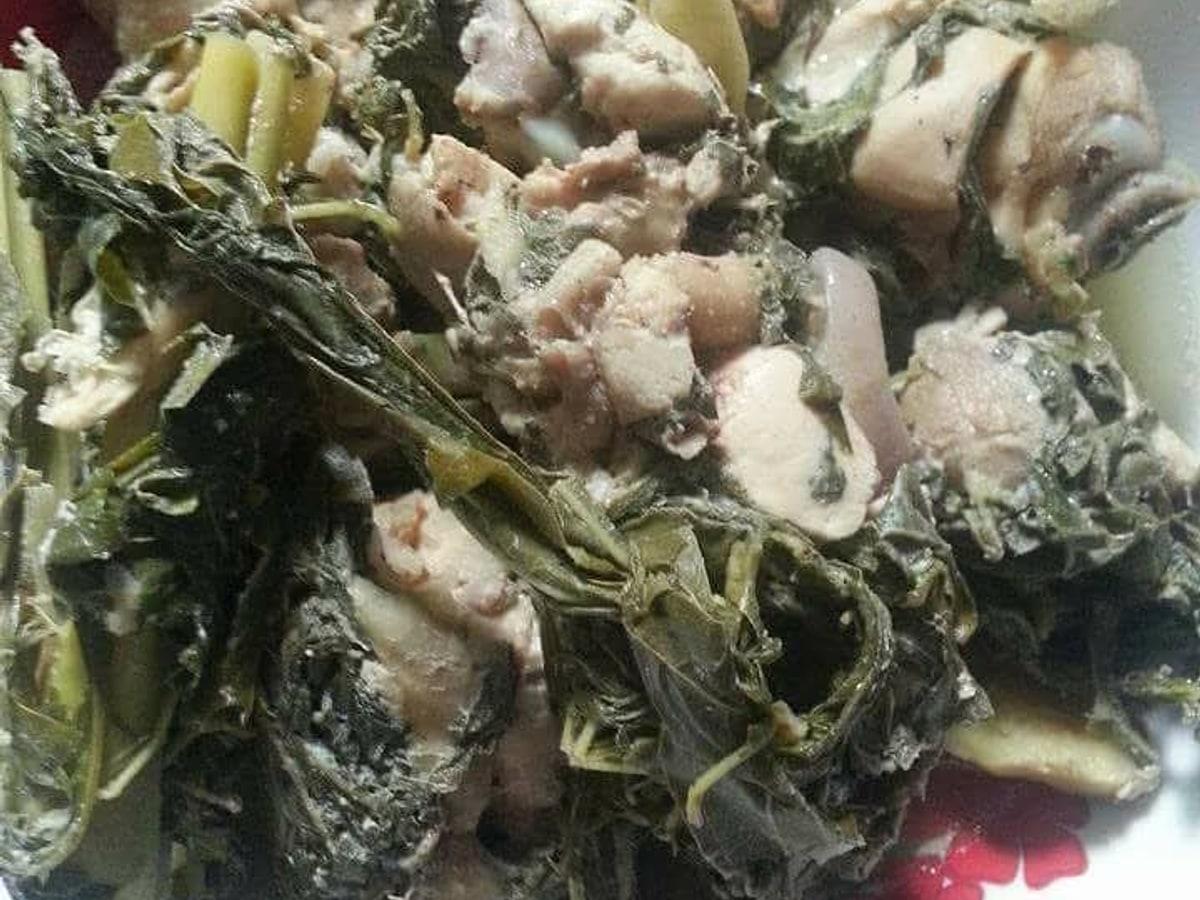 Primer plano de piezas de pollo y verduras de hoja en un guiso cocido en bambú.