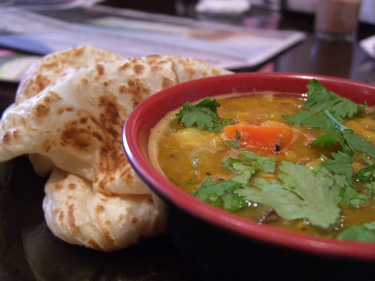 Blätterteigfladenbrotstücke neben einer Schüssel Linsencurry.
