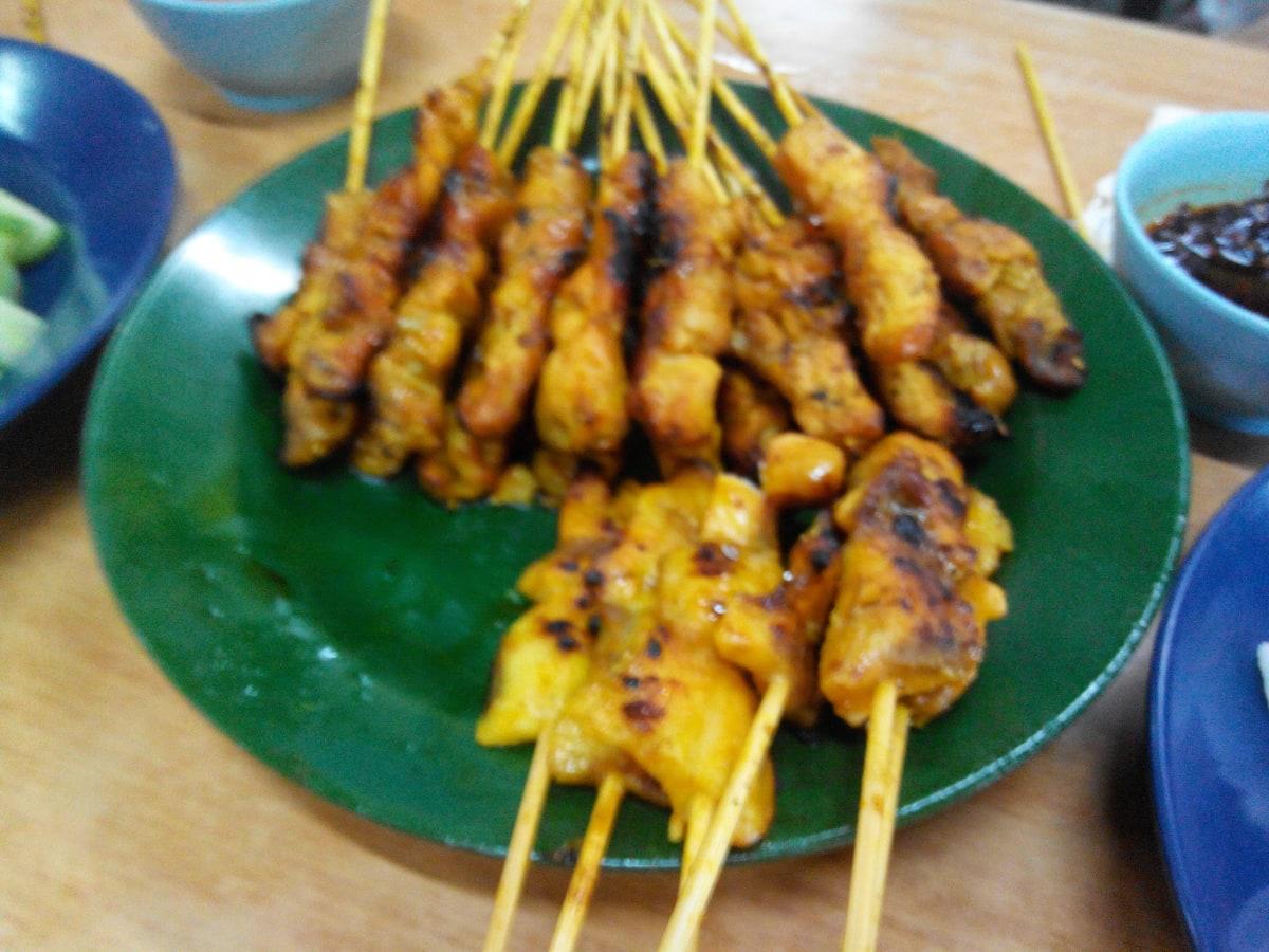 緑の皿にサテの串焼きが置かれ、近くにピーナッツソースがある。