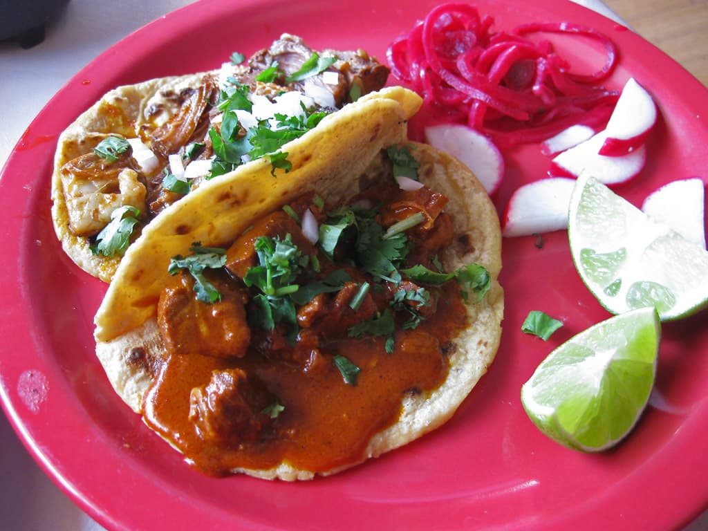 Tacos au porc effiloché rouge achiote avec oignons marinés, radis, citron vert et coriandre.