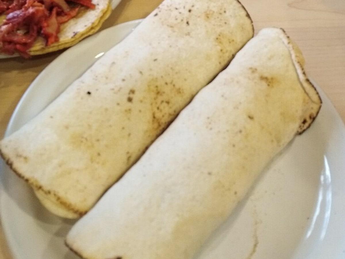 Zwei gefaltete Weizenfladen-Tacos auf einem weißen Teller.