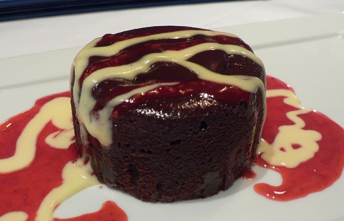 Un pequeño pastel de chocolate glaseado en un plato de postre blanco.