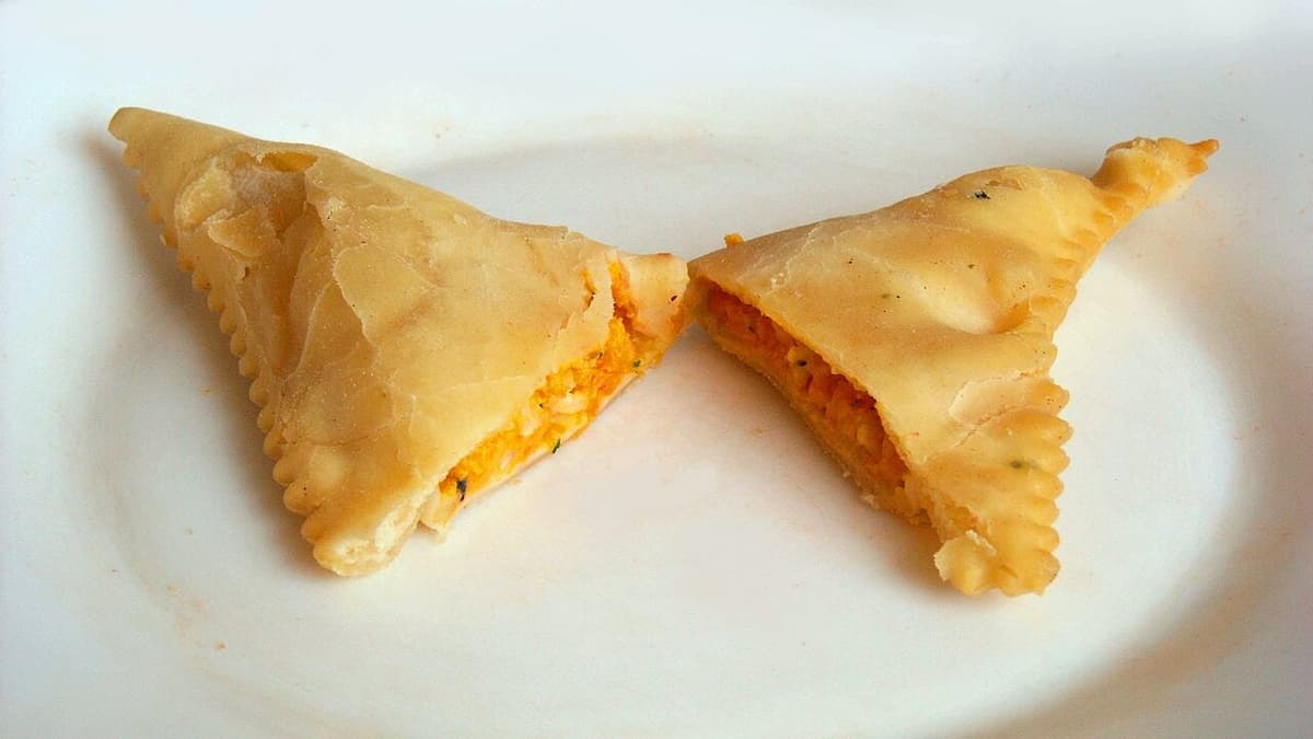 Two triangular fried pastries with orange-green filling on a white plate.