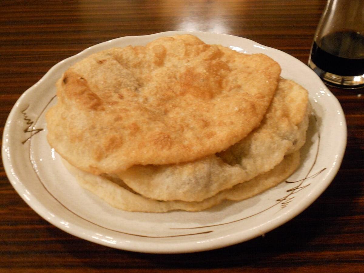 Стопка плоских золотистых жареных мясных пирожков на тарелке.