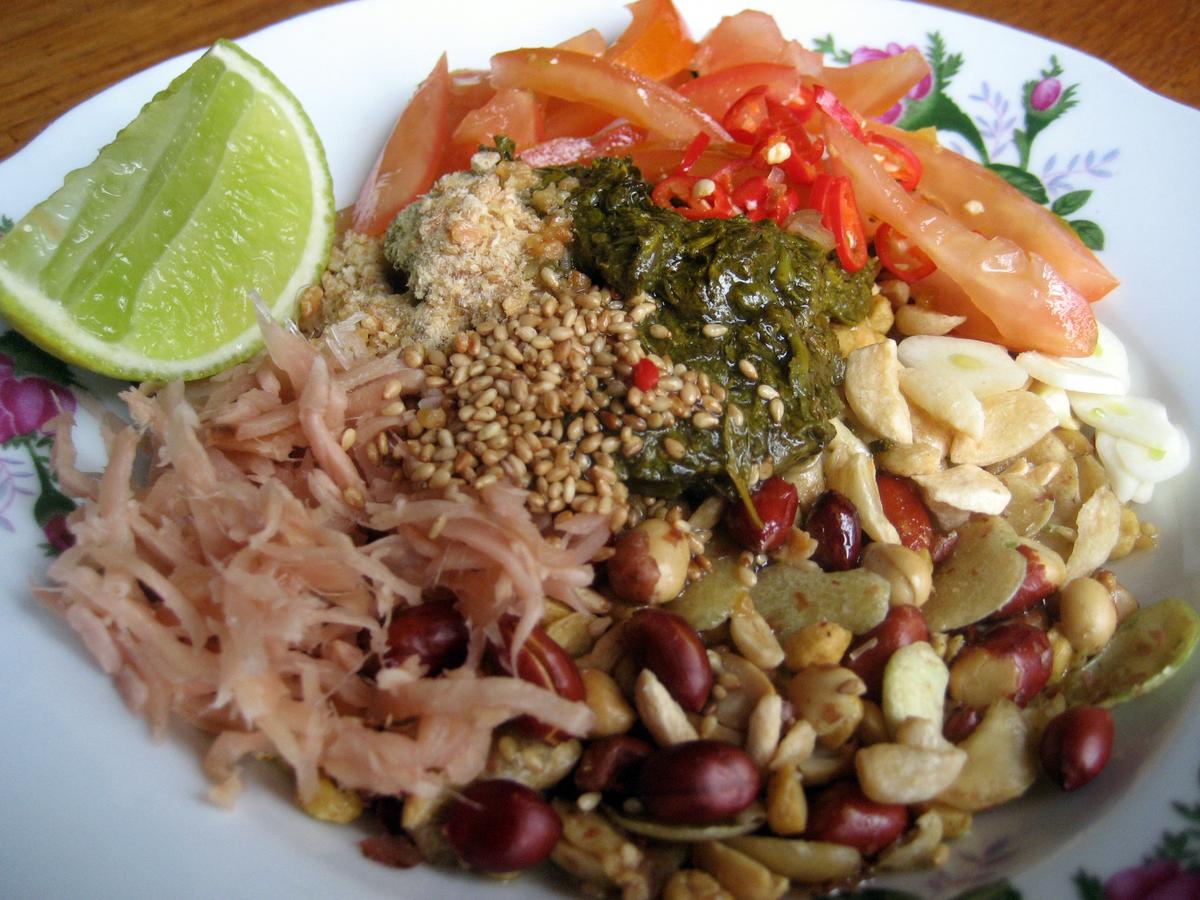 Teeblatt-Salat mit fermentierten Blättern, knusprigen Bohnen, Samen, Tomate, Limette und geriebenem Gemüse.