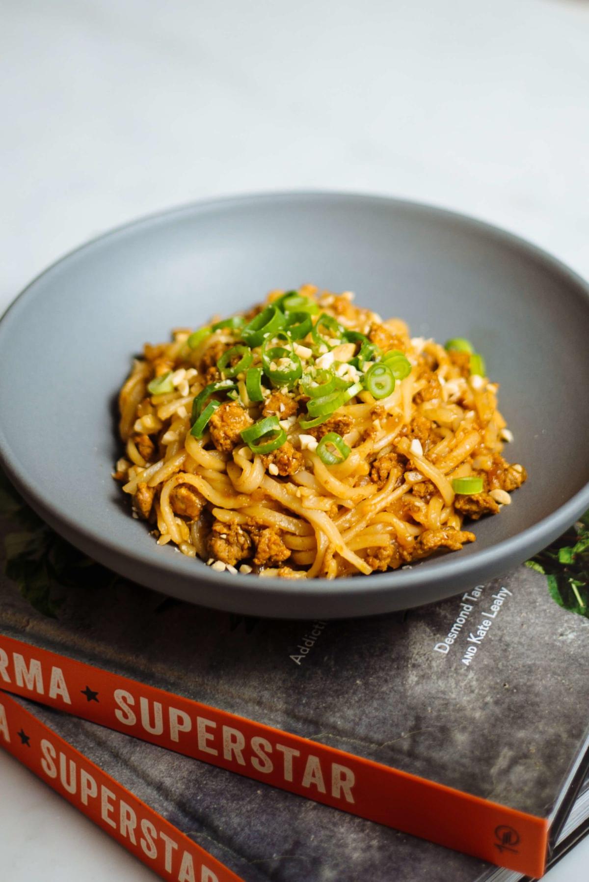 Bowl of sauced rice noodles topped with scallions and minced meat.