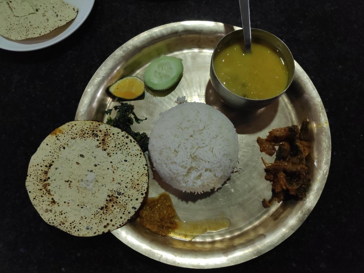 Assiette métallique avec riz, dal de lentilles, légumes verts, cornichons, papad et accompagnements.
