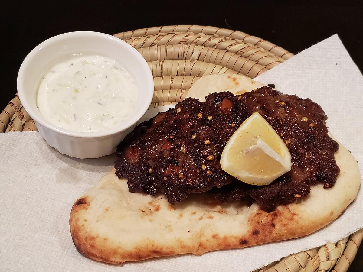 Большая плоская мясная котлета с луком, зеленью, лепешкой и чатни.