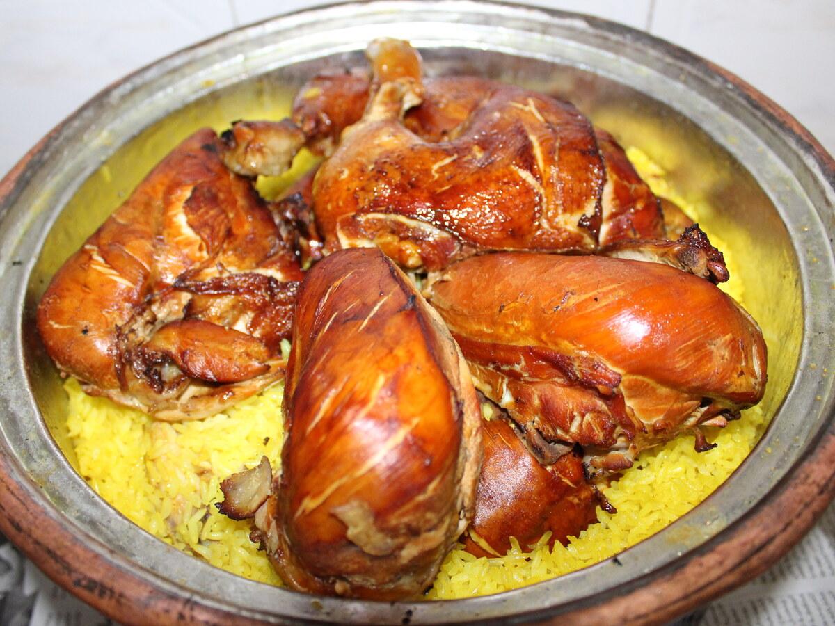 Clay pot filled with yellow rice and browned lamb pieces on top.