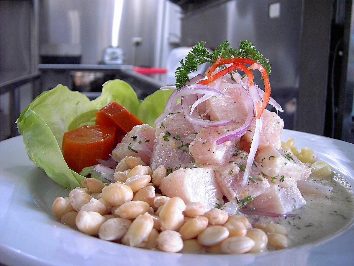 Ceviche de pescado blanco con cebolla, hierbas, pimiento rojo, maíz y lechuga en un plato blanco.