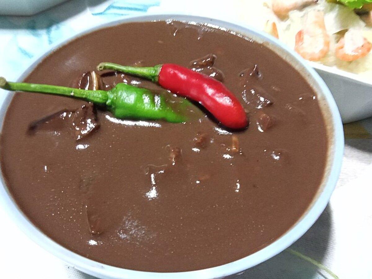 Dunkler glänzender Schweinefleischeintopf in einer Schüssel mit grünen und roten Chilischoten.