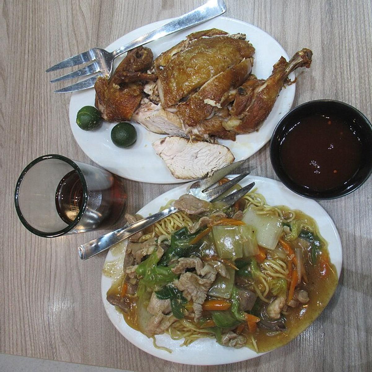 Тарелка жареной лапши с мясом, овощами, вилкой и мисками с соусом.