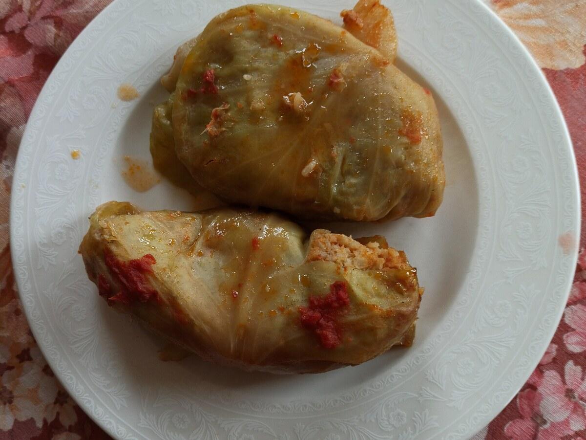 토마토 소스를 곁들인 속을 채운 양배추 롤이 접시에 담겨 있다.