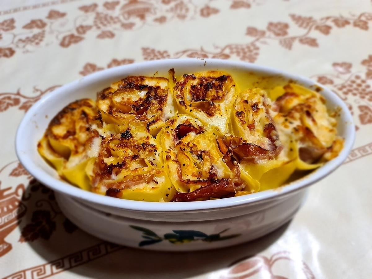 Baked rolled pasta nests with cheese and browned tops in an oval dish.