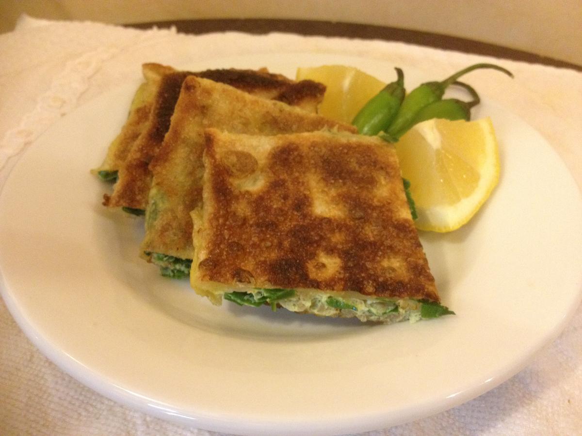 Gebratene gefüllte Fladenbrotstücke auf einem Teller mit Zitrone und grünen Chilis.