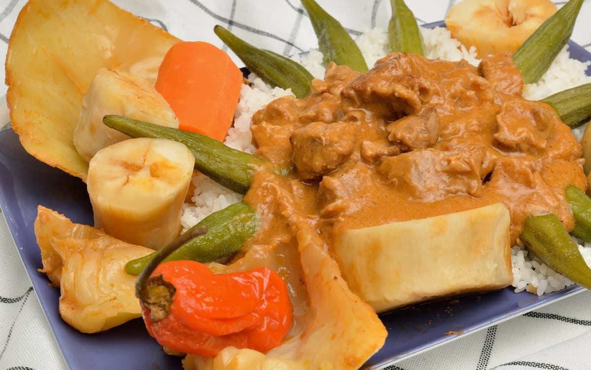 Ensopado de amendoim com legumes e carne servido sobre arroz branco em um prato.