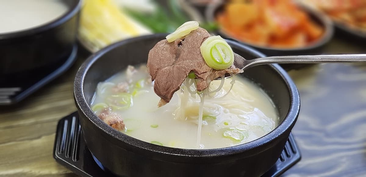 Milky beef bone soup with sliced meat and scallions in a black bowl.