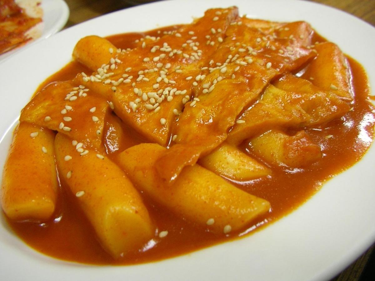 Zähe Reiskuchen und Fischkuchenblätter in glänzender roter Chilisauce mit Sesam.
