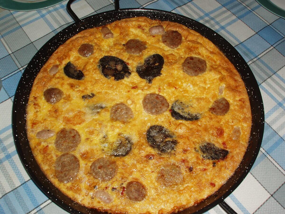 Round pan of baked rice covered with a golden egg crust and sausage pieces.