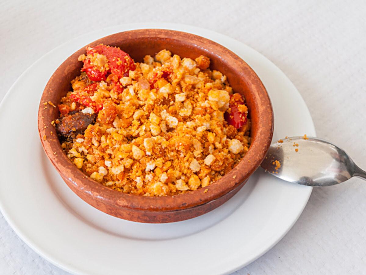 Tontopf mit gebratenen Brotkrumen, roter Paprika und Schweinefleischstücken.