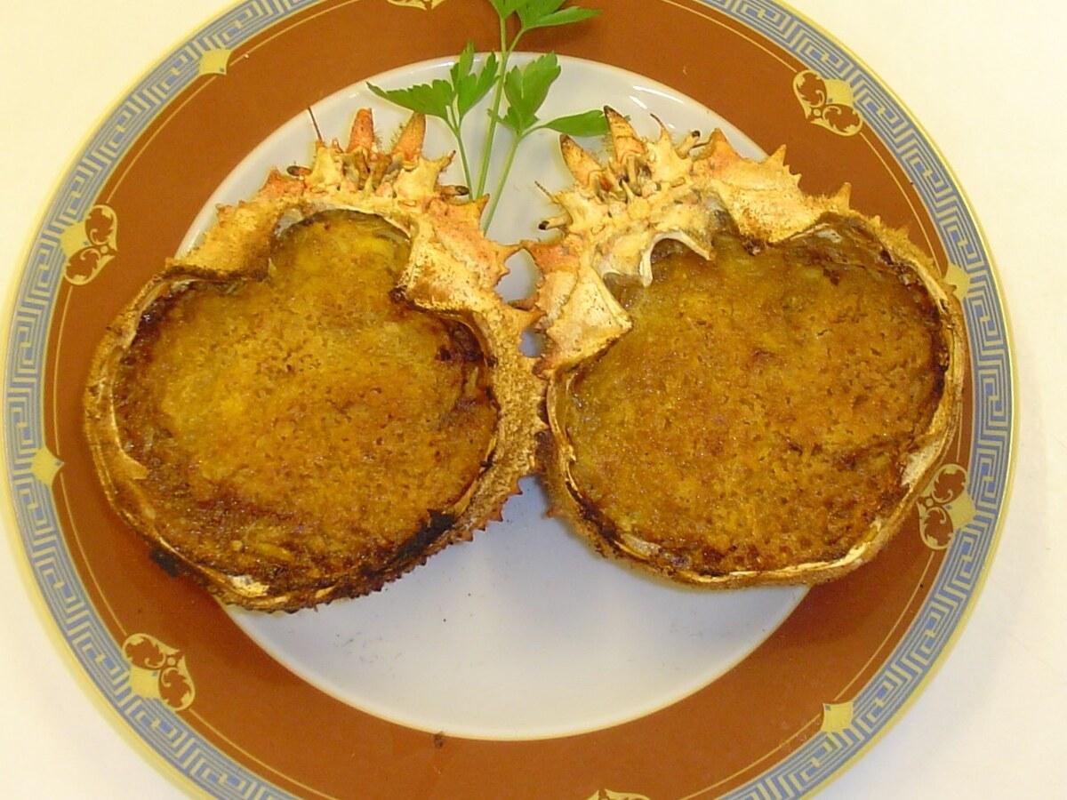 Deux coquilles de crabe farcies et gratinées sur une assiette à motifs.