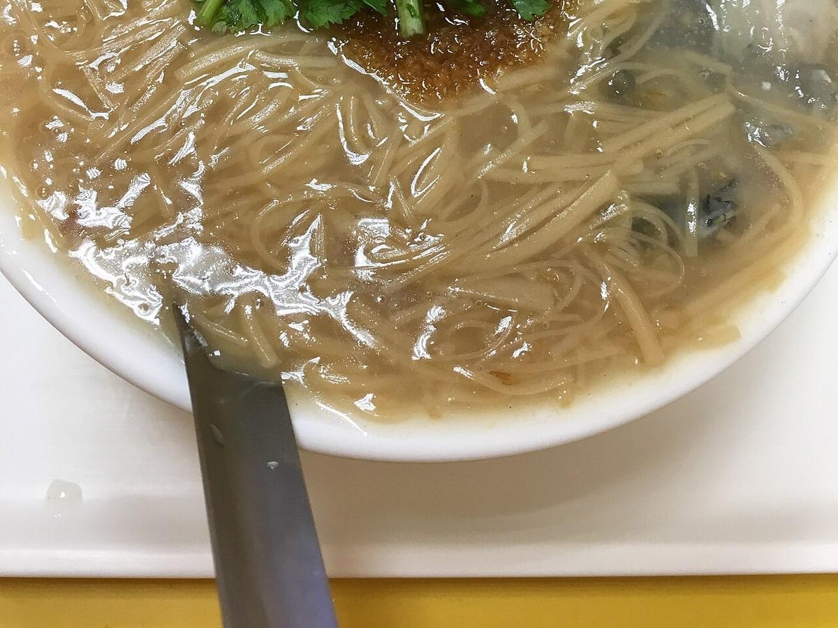 Close-up mangkuk sup mie kental dengan tiram dan sendok.
