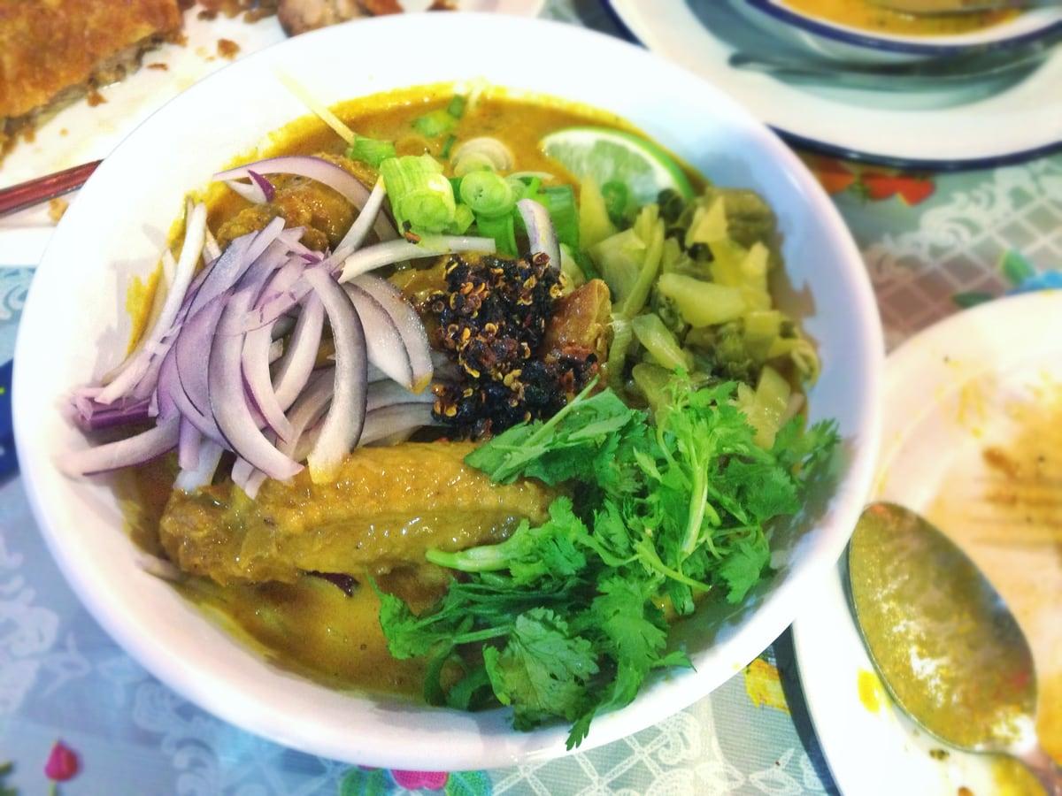 Tazón de sopa de pollo con fideos al curry cubierto con fideos crujientes, cebolla, hierbas y lima.