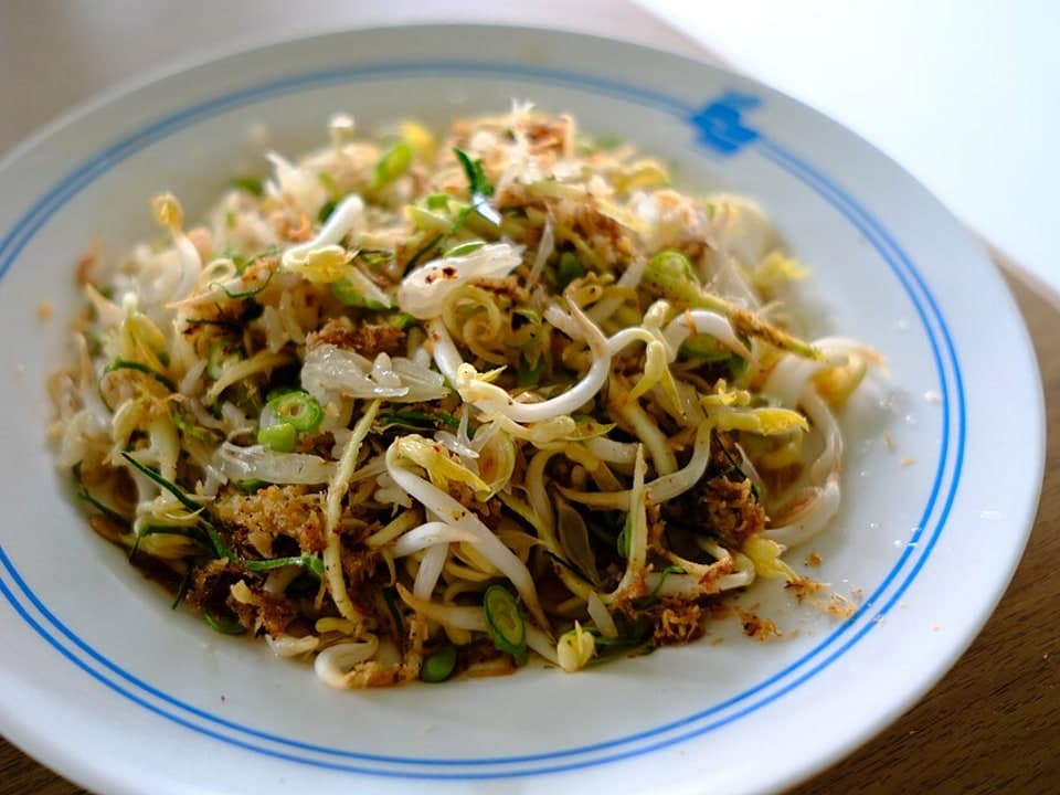 Gemischter Reissalat mit zerkleinerten Kräutern, Bohnensprossen und gerösteter Kokosnuss auf einem Teller.