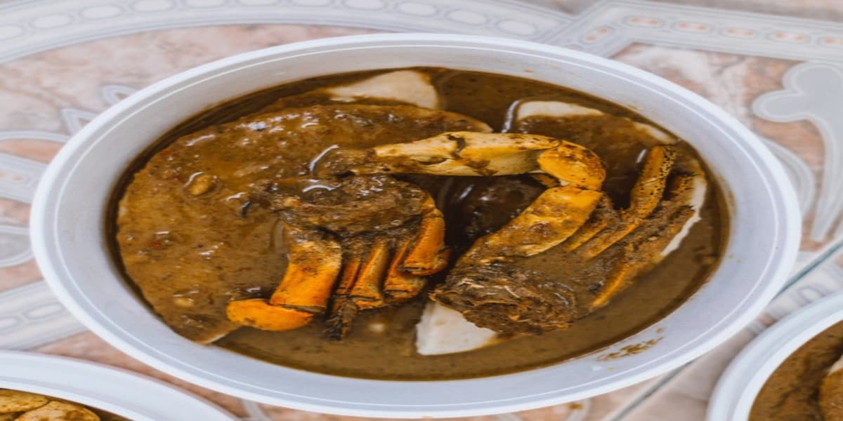 Capit kepiting kari dan dumpling pucat dalam mangkuk dangkal untuk dibawa pulang.