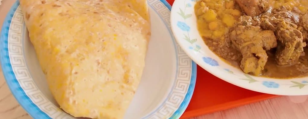 Pão achatado ao lado de um prato de curry de frango com grão-de-bico e batatas.