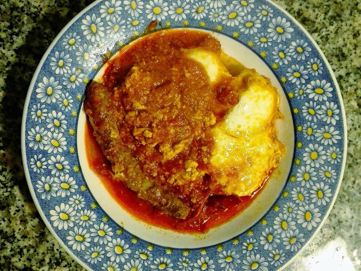 Teller mit roter Tomaten-Paprika-Sauce mit Eiern und geschnittener würziger Wurst.