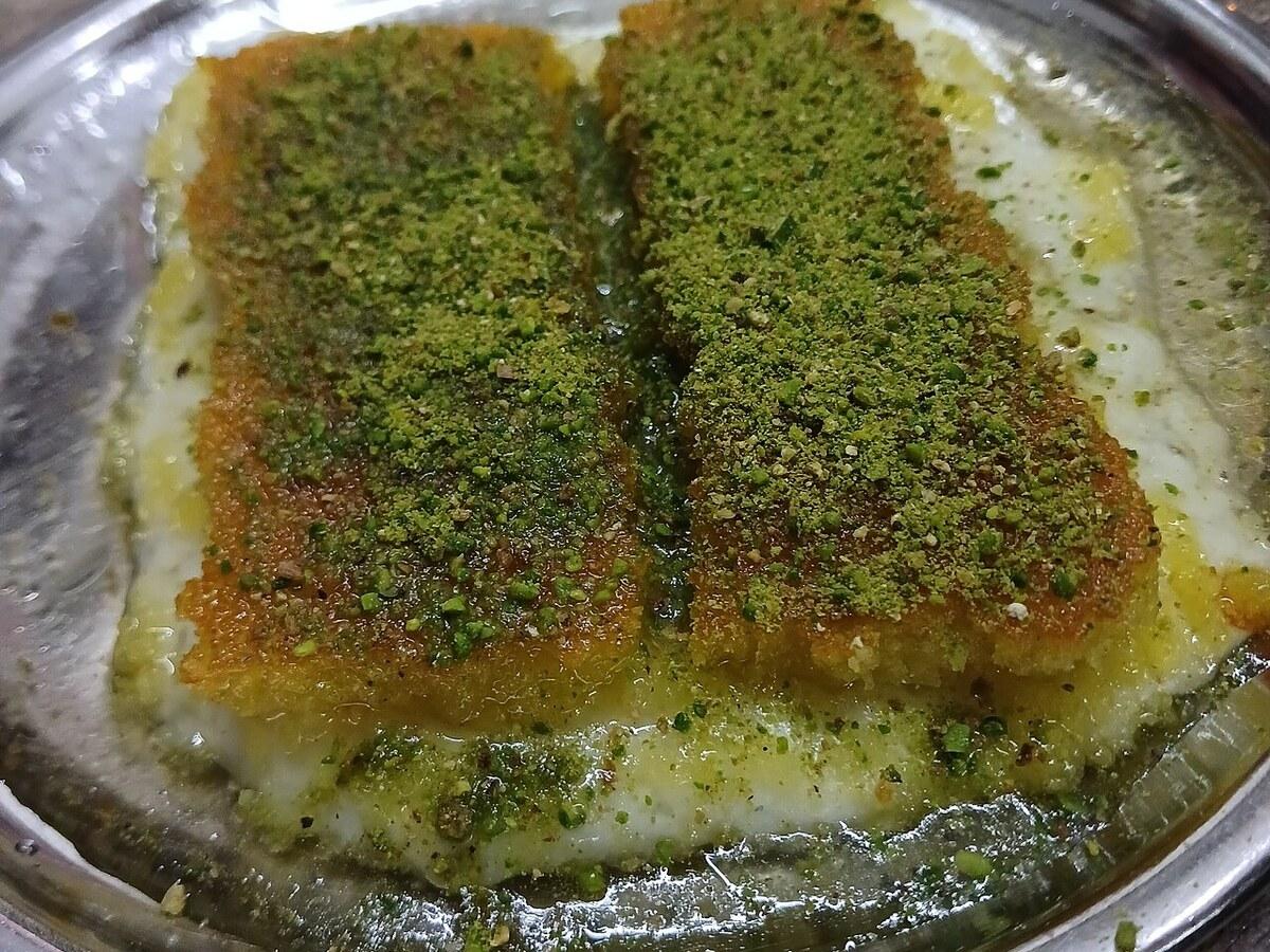 Два прямоугольных куска тонкой лапши, покрытые измельчёнными фисташками в металлическом подносе.