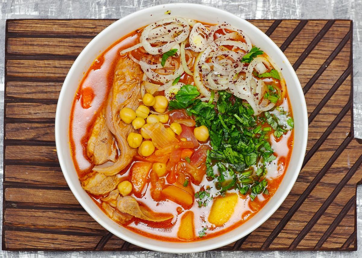 Schüssel mit klarer Fleischsuppe mit Kartoffeln, Karotten, Zwiebeln, Kräutern und Fleischstücken.