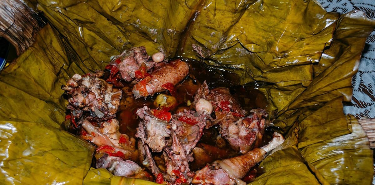 Potongan ayam dan kuahnya dibuka di dalam daun pisang matang yang mengilap.