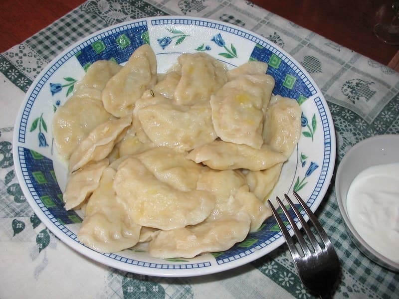 Teller mit blassen Halbmondteigtaschen, begleitet von einer kleinen Schale Sauerrahm.