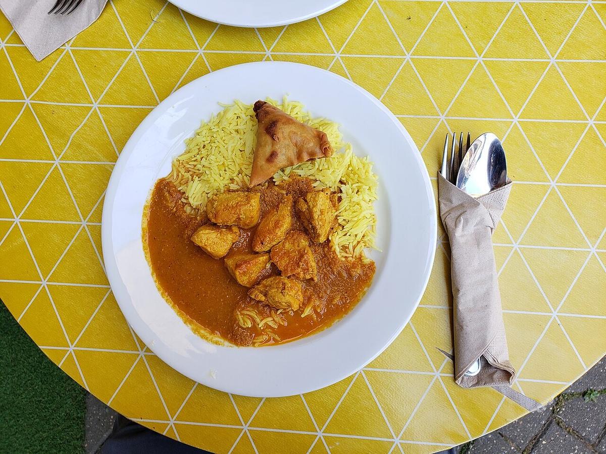Hühnerstücke in orangefarbener Currysauce mit gelbem Reis und dreieckigem Snack auf einem weißen Teller.