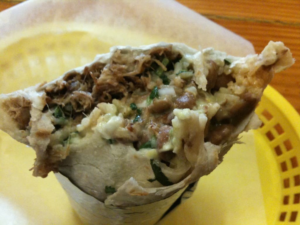 Aufgeschnittener in Alufolie eingewickelter Burrito, der Fleisch, Bohnen, Reis und Salsa zeigt.