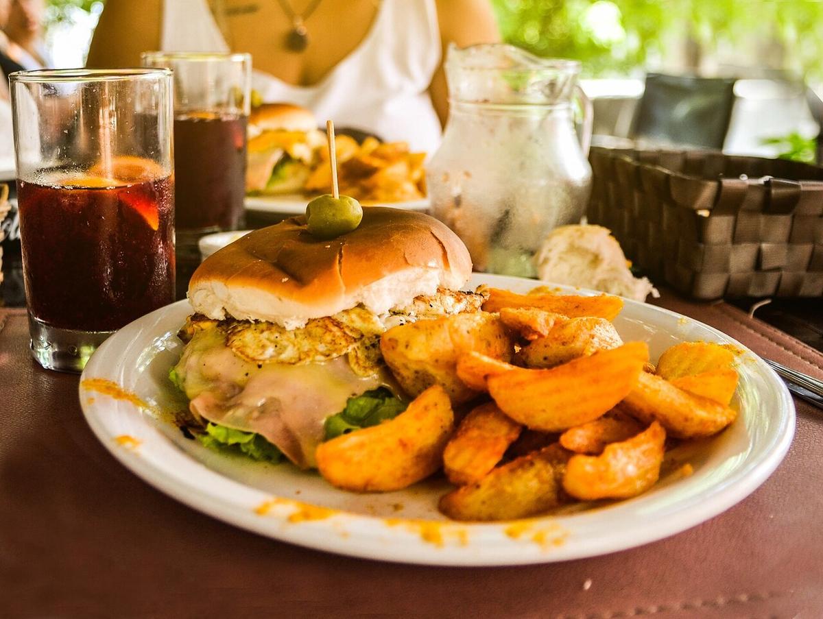 Sándwich de carne con huevo, queso, jamón, lechuga, tomate, aceituna y papas fritas en un plato.