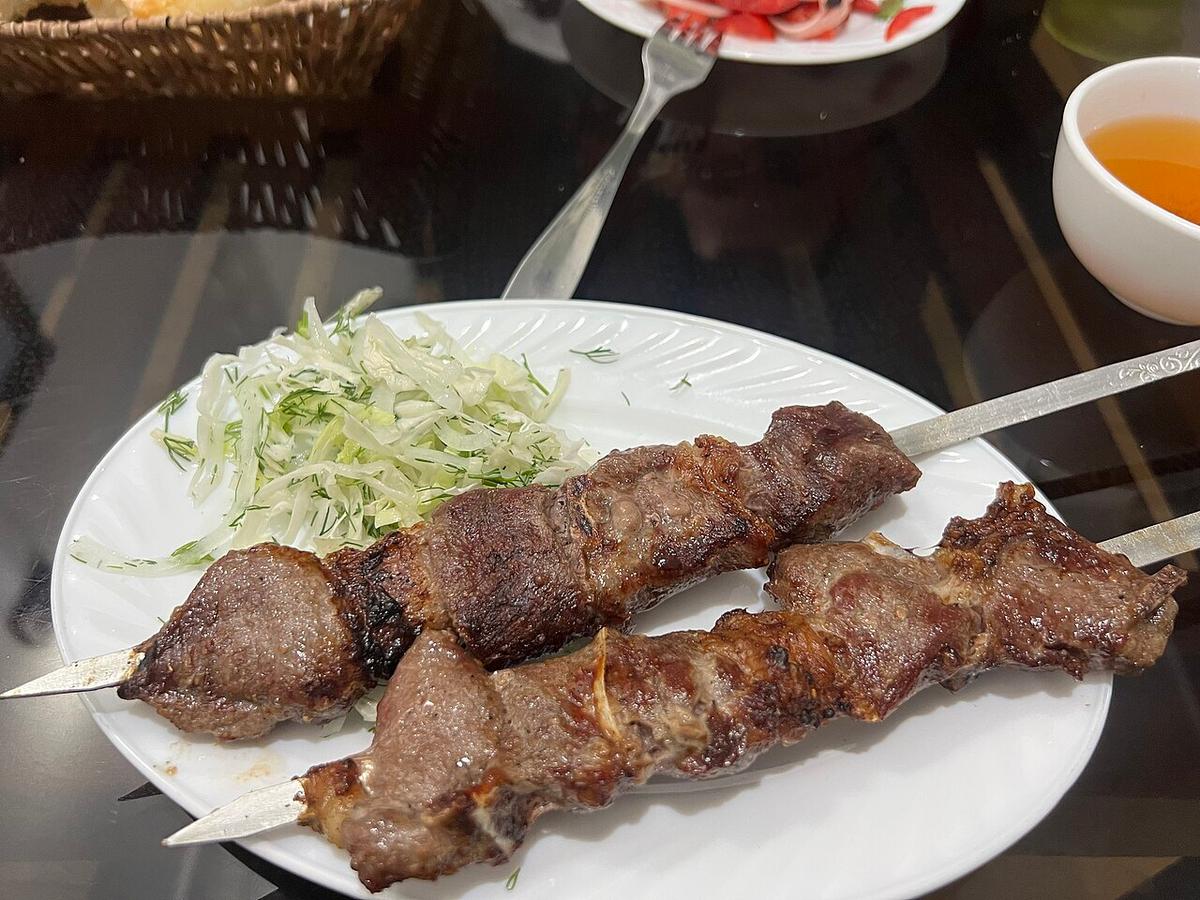 Zwei gegrillte Fleischspieße auf einem weißen Teller mit geraspeltem Kohl und Tee daneben.