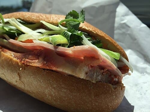 Sandwich avec baguette croustillante, garnie de viande tranchée, légumes et herbes.