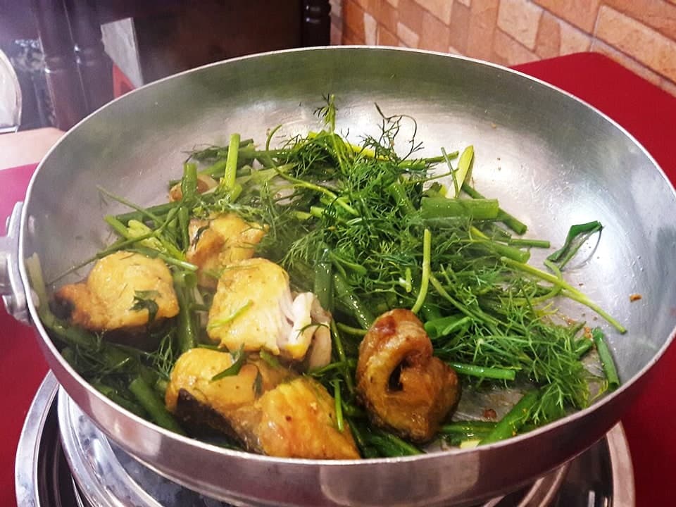 Mit Kurkuma marinierter Fisch mit Dill und Frühlingszwiebeln, der in einer Metallpfanne brät.